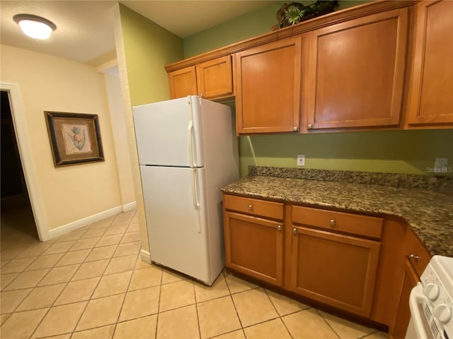 kitchen with light tile floors, dark stone counters, stove, and white refrigerator