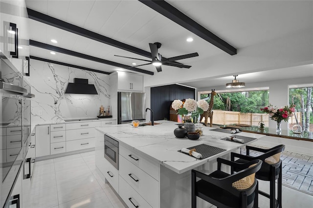 kitchen with appliances with stainless steel finishes, tasteful backsplash, beam ceiling, white cabinets, and a large island