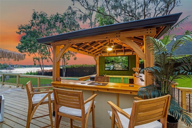 deck at dusk with a bar, a water view, and a gazebo