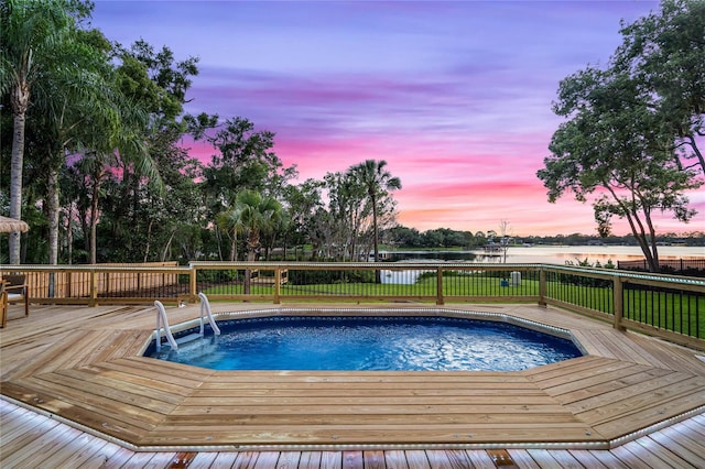 pool at dusk featuring a deck with water view