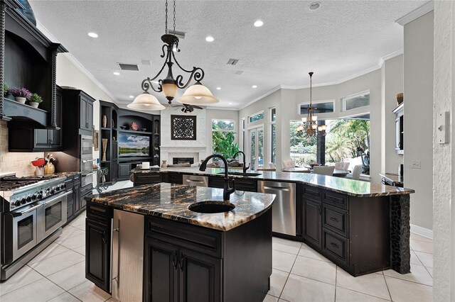 kitchen featuring a center island with sink, stainless steel appliances, hanging light fixtures, and a textured ceiling