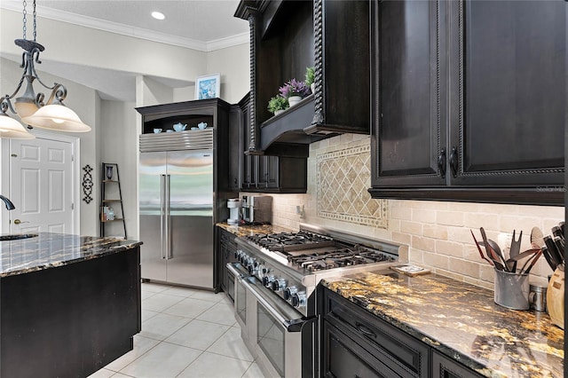 kitchen featuring sink, dark stone countertops, pendant lighting, light tile patterned floors, and high end appliances