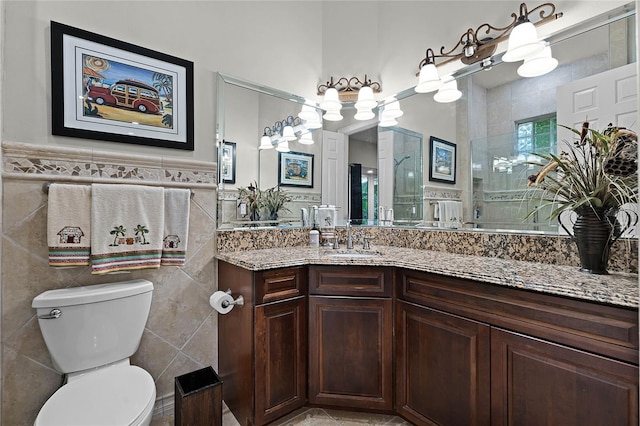 bathroom with a shower with door, vanity, tile walls, and toilet