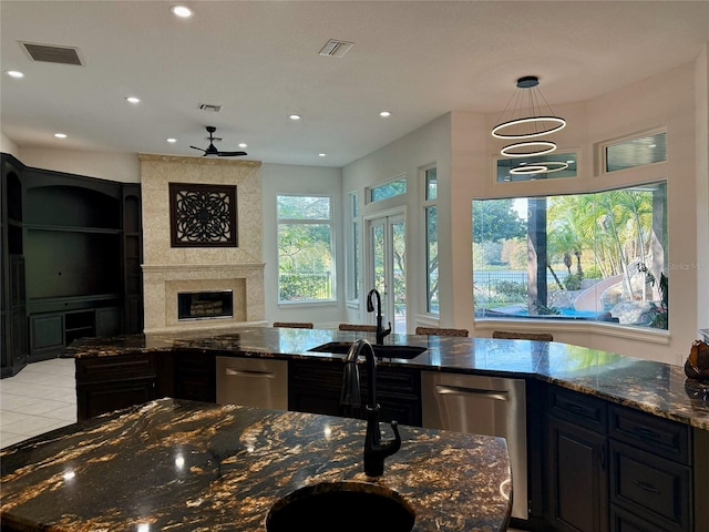 kitchen featuring a large fireplace, sink, dark stone countertops, dishwasher, and hanging light fixtures