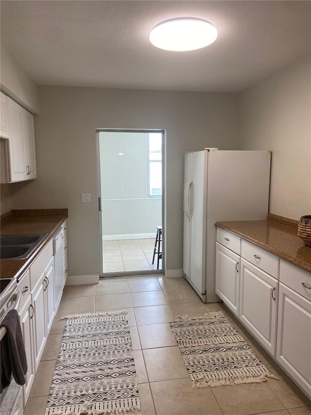 kitchen featuring white refrigerator with ice dispenser, sink, electric range, light tile patterned floors, and white cabinetry