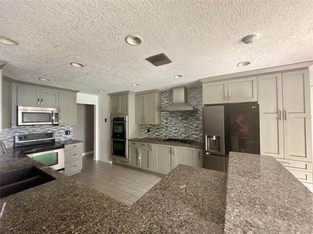 kitchen featuring tasteful backsplash, tile floors, a textured ceiling, wall chimney range hood, and appliances with stainless steel finishes