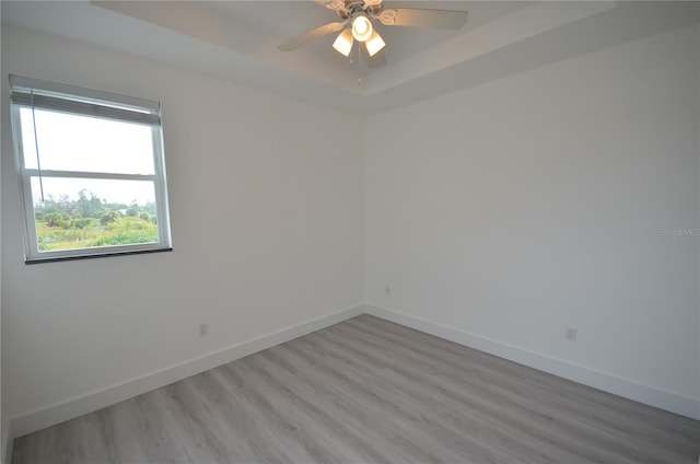 spare room with baseboards, a ceiling fan, wood finished floors, and a raised ceiling