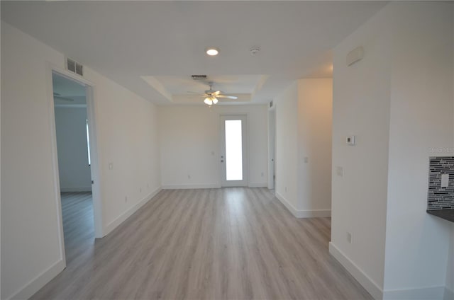 unfurnished room featuring a ceiling fan, light wood-style floors, a tray ceiling, baseboards, and visible vents