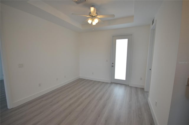 spare room with light wood finished floors, baseboards, visible vents, and a raised ceiling