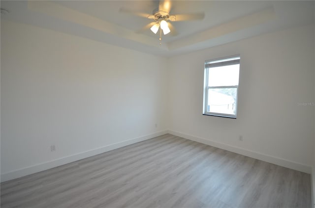 unfurnished room featuring ceiling fan, baseboards, a tray ceiling, and light wood-style floors