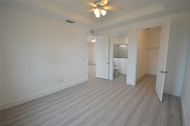 unfurnished bedroom featuring a spacious closet, a raised ceiling, visible vents, light wood-style floors, and baseboards