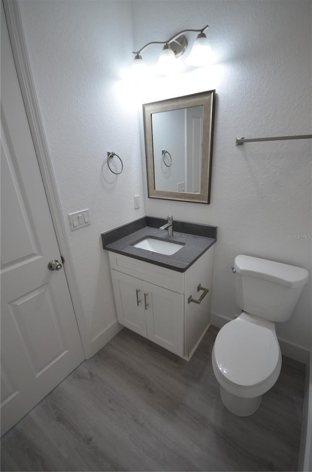 bathroom with baseboards, wood finished floors, vanity, and toilet