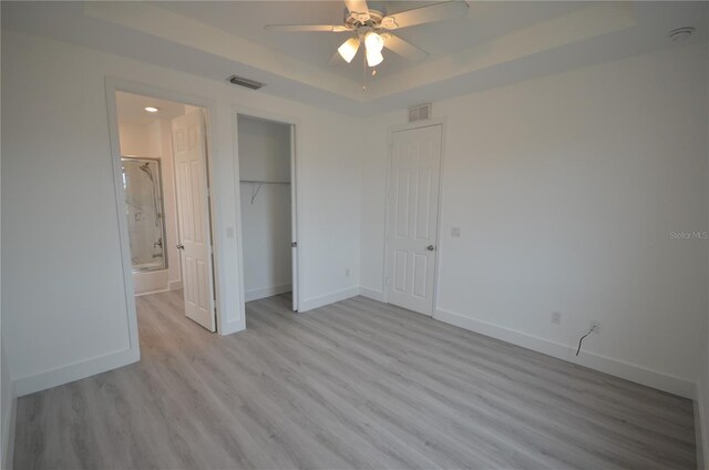 unfurnished bedroom featuring baseboards, light wood-style flooring, visible vents, and a raised ceiling