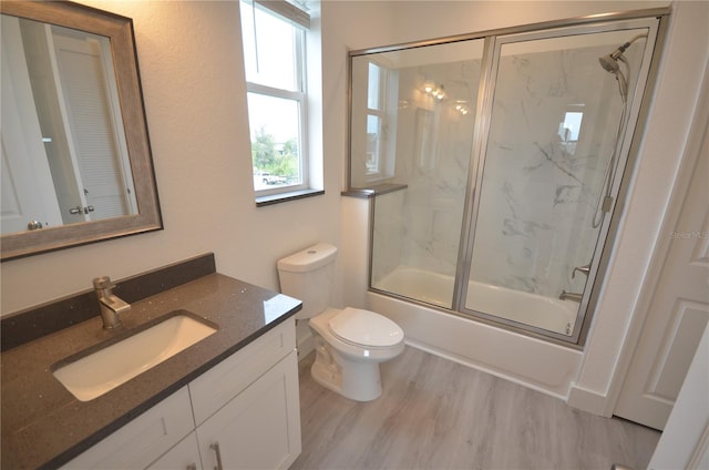 full bath featuring combined bath / shower with glass door, wood finished floors, vanity, and toilet