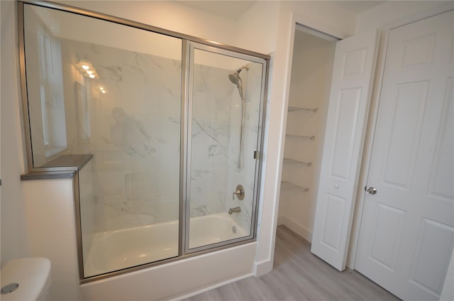bathroom with toilet, wood finished floors, and combined bath / shower with glass door