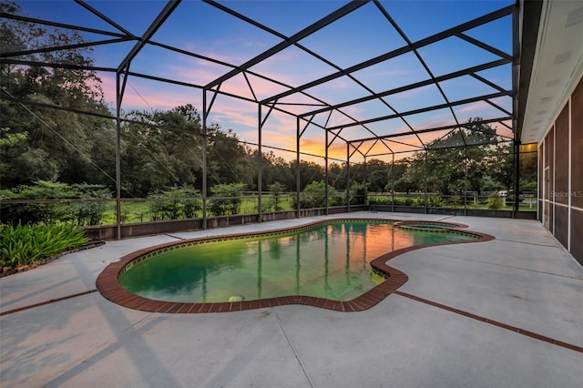 pool at dusk featuring a lanai, a patio, and an in ground hot tub