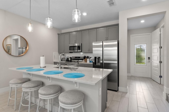 kitchen featuring gray cabinetry, decorative light fixtures, stainless steel appliances, and an island with sink