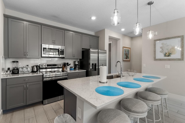 kitchen featuring gray cabinetry, sink, an island with sink, decorative light fixtures, and stainless steel appliances