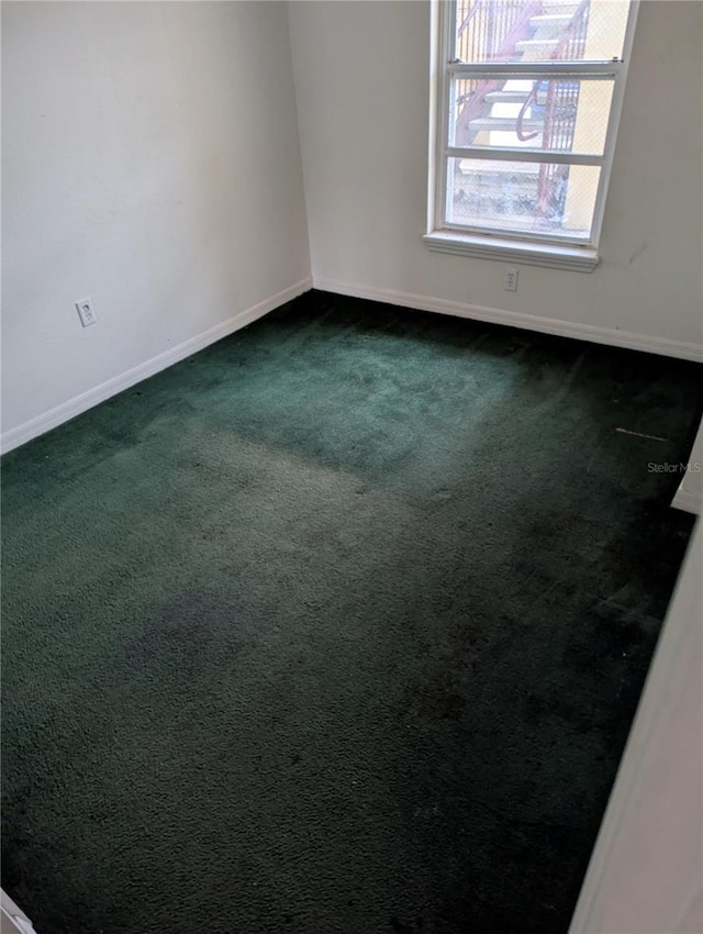 empty room featuring baseboards and dark colored carpet