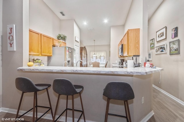 kitchen with kitchen peninsula, a breakfast bar, stainless steel appliances, and light hardwood / wood-style flooring