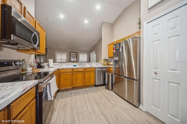 kitchen with sink, kitchen peninsula, lofted ceiling, appliances with stainless steel finishes, and light wood-type flooring