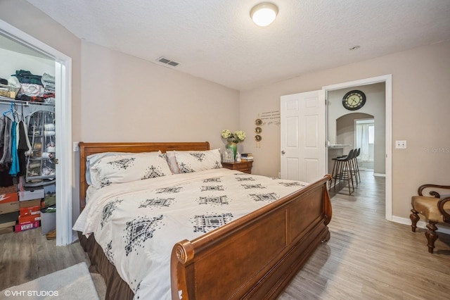 bedroom with wood-type flooring, a walk in closet, a textured ceiling, and a closet