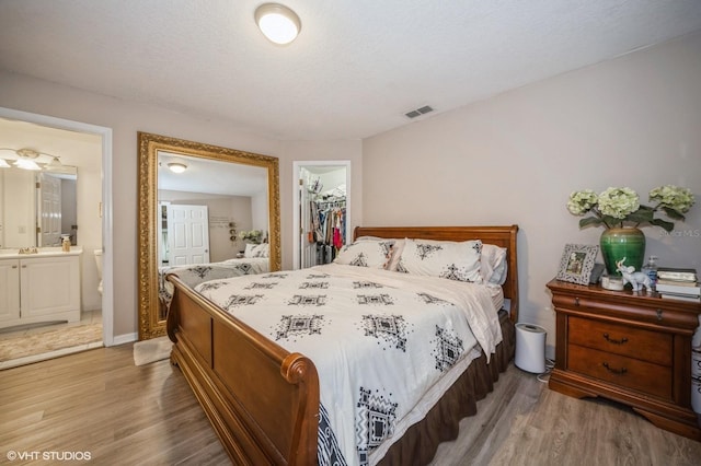 bedroom featuring a walk in closet, ensuite bathroom, sink, dark hardwood / wood-style floors, and a closet