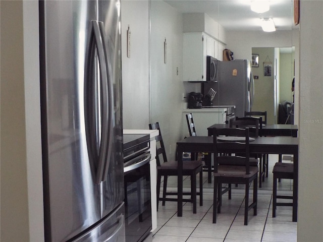 kitchen featuring white cabinets, stainless steel fridge, light tile flooring, and range