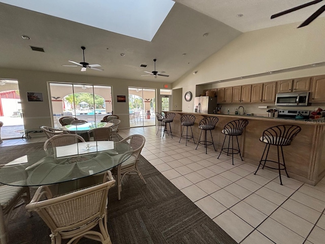 dining room with light tile patterned flooring, a healthy amount of sunlight, a skylight, and high vaulted ceiling