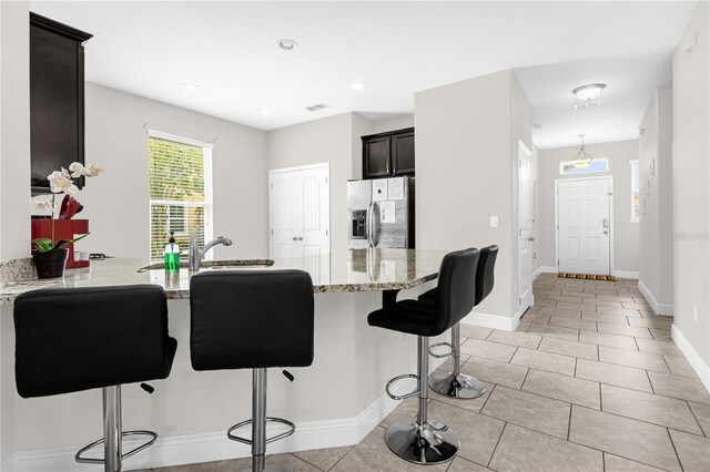 kitchen featuring light tile patterned flooring, kitchen peninsula, a kitchen breakfast bar, light stone countertops, and stainless steel fridge