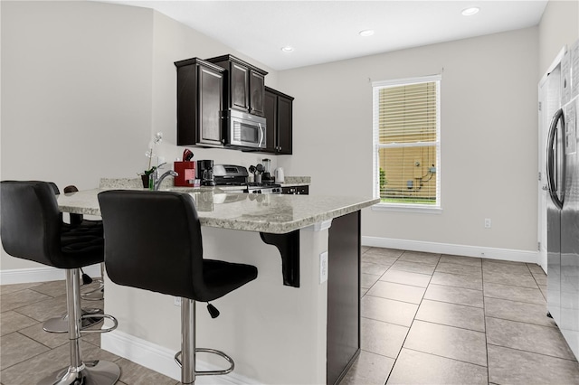 kitchen featuring light stone countertops, light tile patterned flooring, appliances with stainless steel finishes, and a breakfast bar