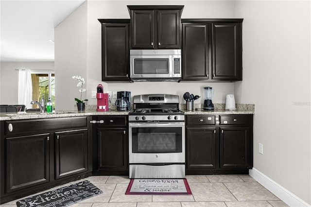 kitchen featuring stainless steel appliances, light stone countertops, sink, and light tile patterned floors