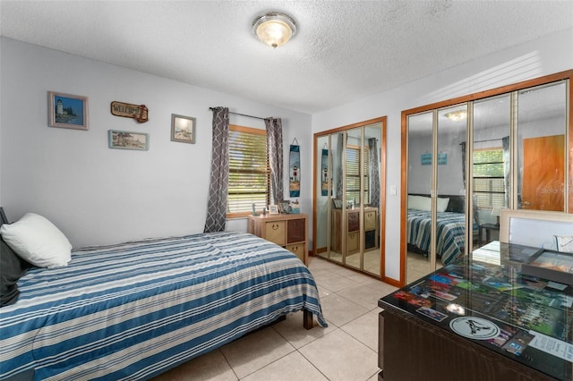 tiled bedroom with a textured ceiling, two closets, and multiple windows