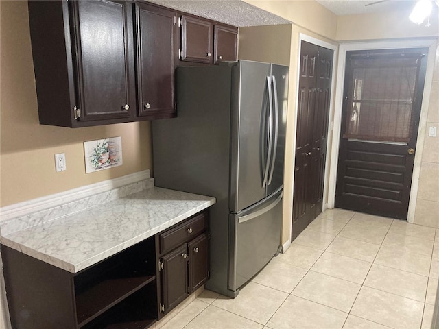 kitchen with ceiling fan, stainless steel fridge, a textured ceiling, dark brown cabinets, and light tile patterned flooring