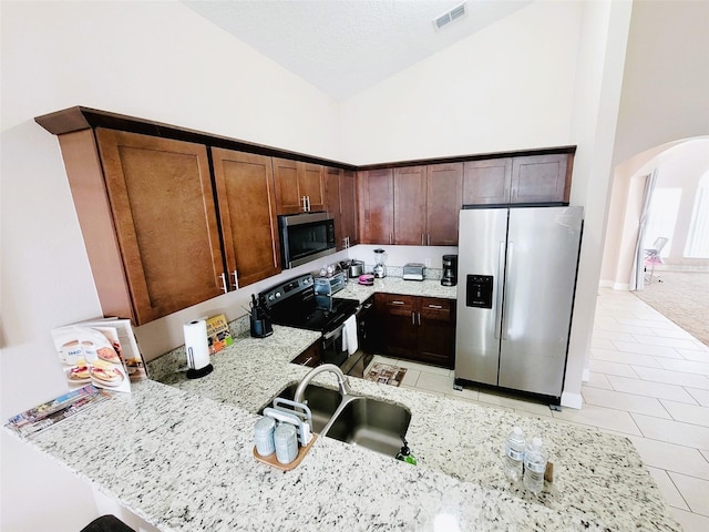 kitchen with high vaulted ceiling, sink, appliances with stainless steel finishes, and light stone countertops