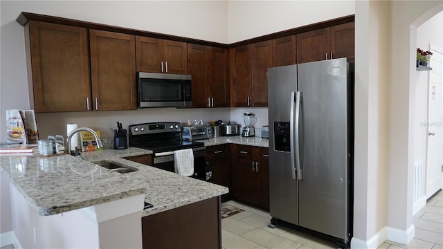 kitchen featuring light tile patterned floors, appliances with stainless steel finishes, dark brown cabinets, light stone countertops, and sink