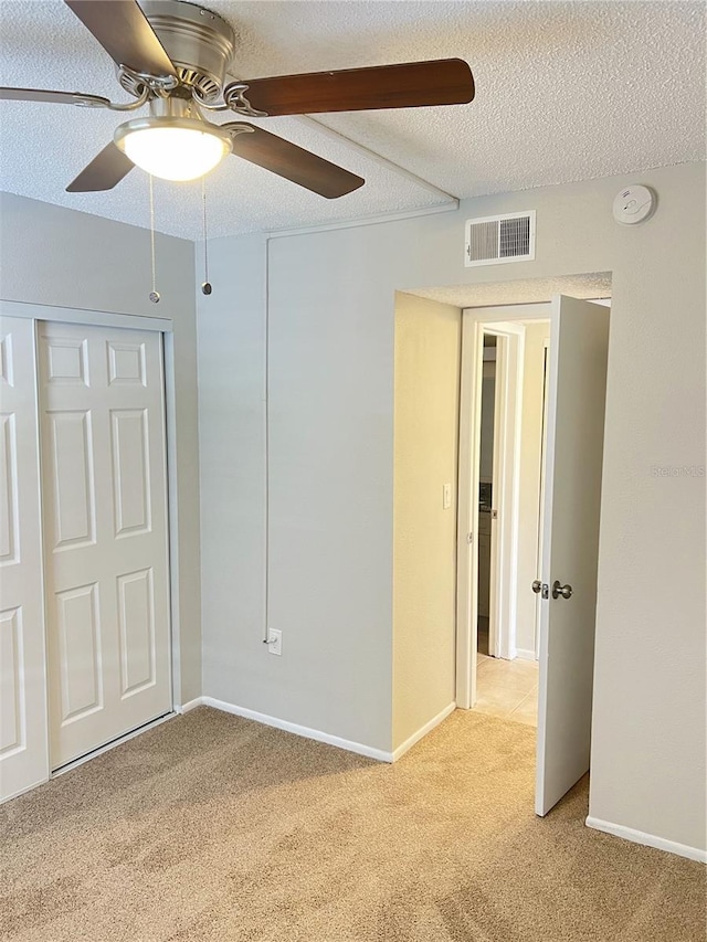 unfurnished bedroom with ceiling fan, a closet, a textured ceiling, and light colored carpet