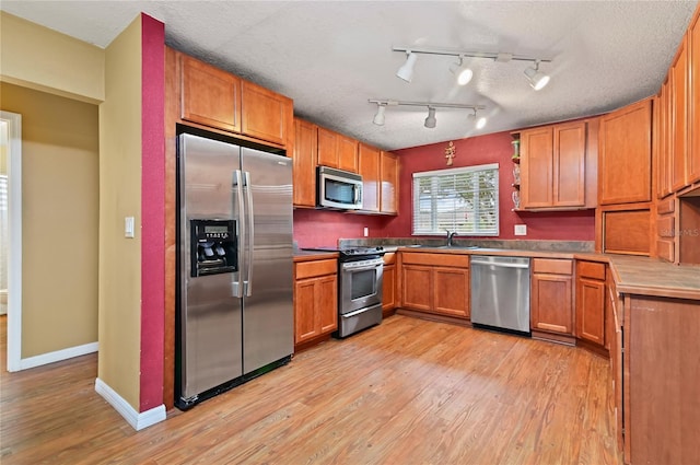 kitchen with a textured ceiling, light hardwood / wood-style flooring, stainless steel appliances, rail lighting, and sink