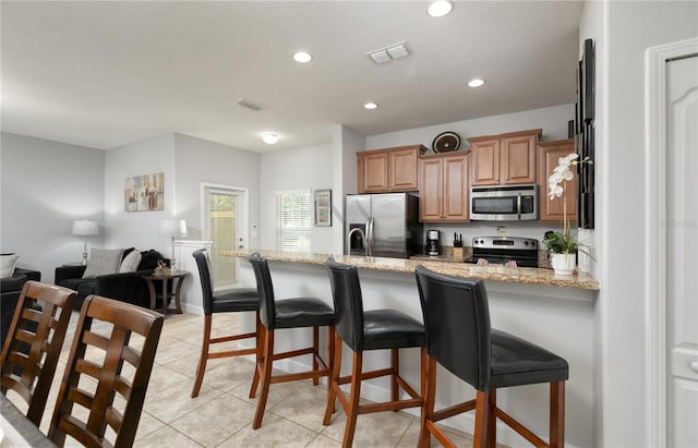 kitchen with a peninsula, a kitchen bar, stainless steel appliances, visible vents, and light stone counters