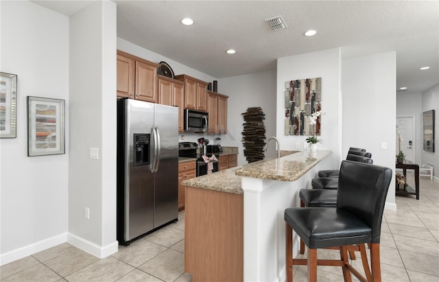 kitchen with light stone counters, kitchen peninsula, stainless steel appliances, a kitchen breakfast bar, and light tile floors