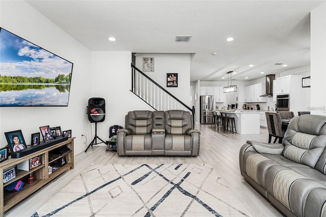 living area featuring a textured ceiling, light wood-style flooring, recessed lighting, visible vents, and stairway