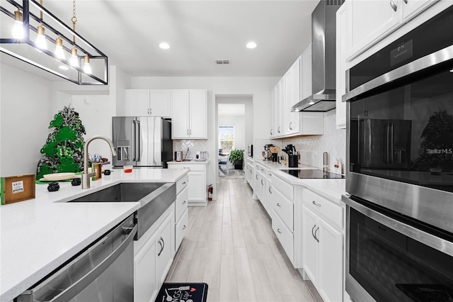 kitchen with visible vents, wall chimney exhaust hood, appliances with stainless steel finishes, light countertops, and a sink