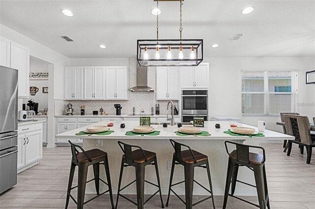 kitchen featuring visible vents, a breakfast bar, stainless steel appliances, light countertops, and wall chimney range hood