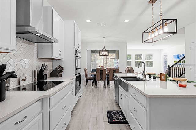 kitchen with white cabinets, decorative light fixtures, black electric stovetop, light countertops, and wall chimney range hood