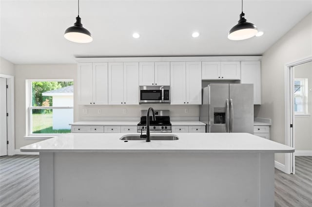 kitchen with stainless steel appliances, sink, white cabinetry, an island with sink, and pendant lighting