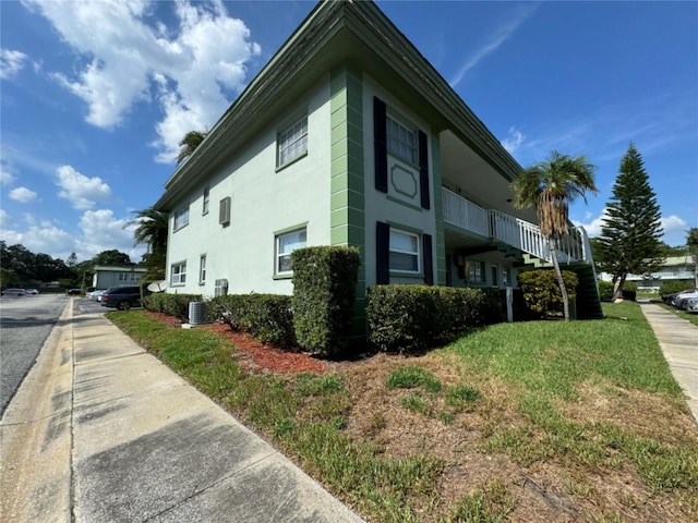 view of side of property featuring cooling unit, a yard, and stucco siding