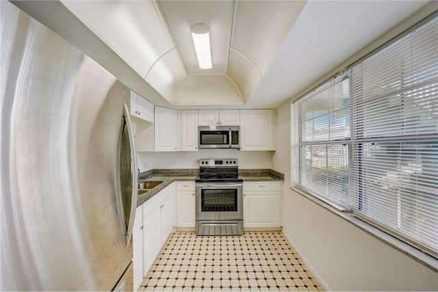 kitchen featuring dark stone countertops, appliances with stainless steel finishes, white cabinets, light tile floors, and a raised ceiling