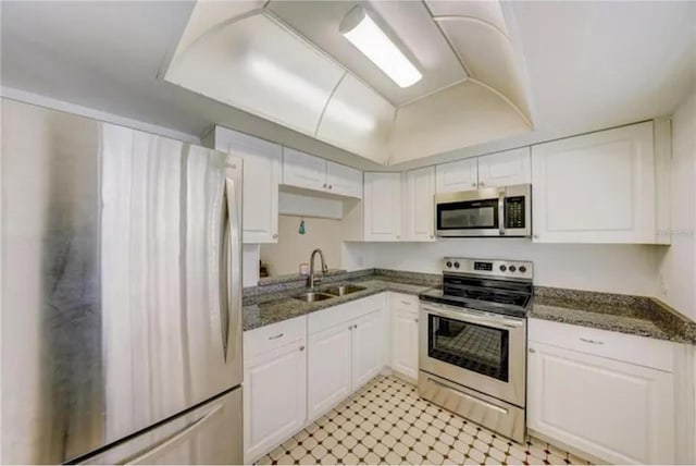 kitchen featuring a tray ceiling, dark stone counters, a sink, stainless steel appliances, and white cabinets