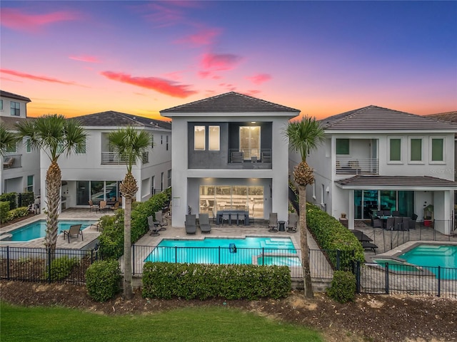 back house at dusk with a fenced in pool, a balcony, and a patio