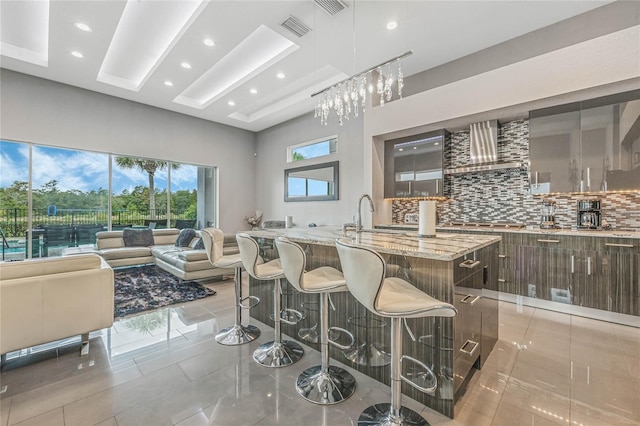 interior space featuring light stone countertops, a high ceiling, wall chimney range hood, tasteful backsplash, and light tile patterned floors